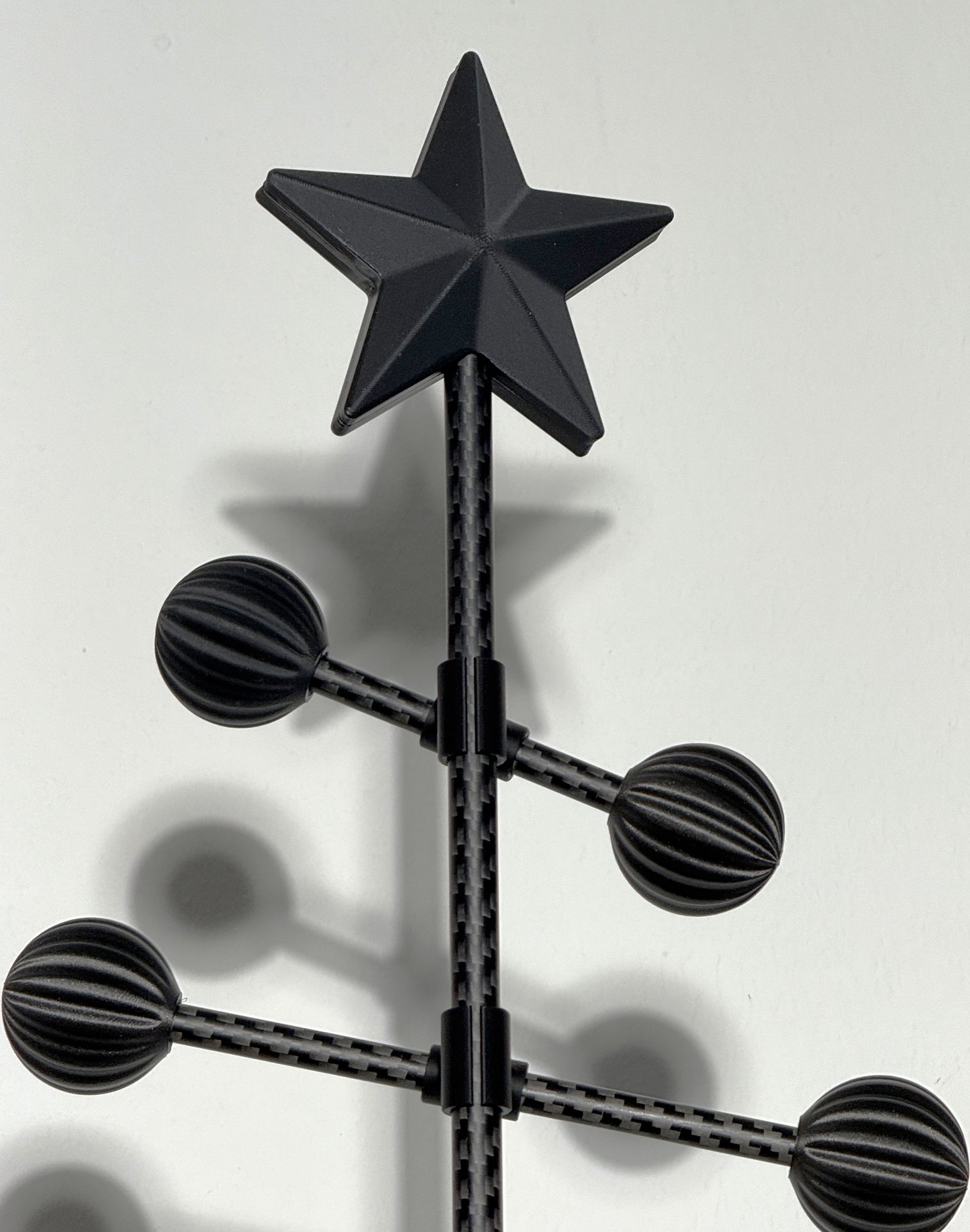 Schwarzer Metall-Weihnachtsbaum mit 3D-gedrucktem Stern als Baumspitze und schwarzen Kugeln auf weißem Hintergrund