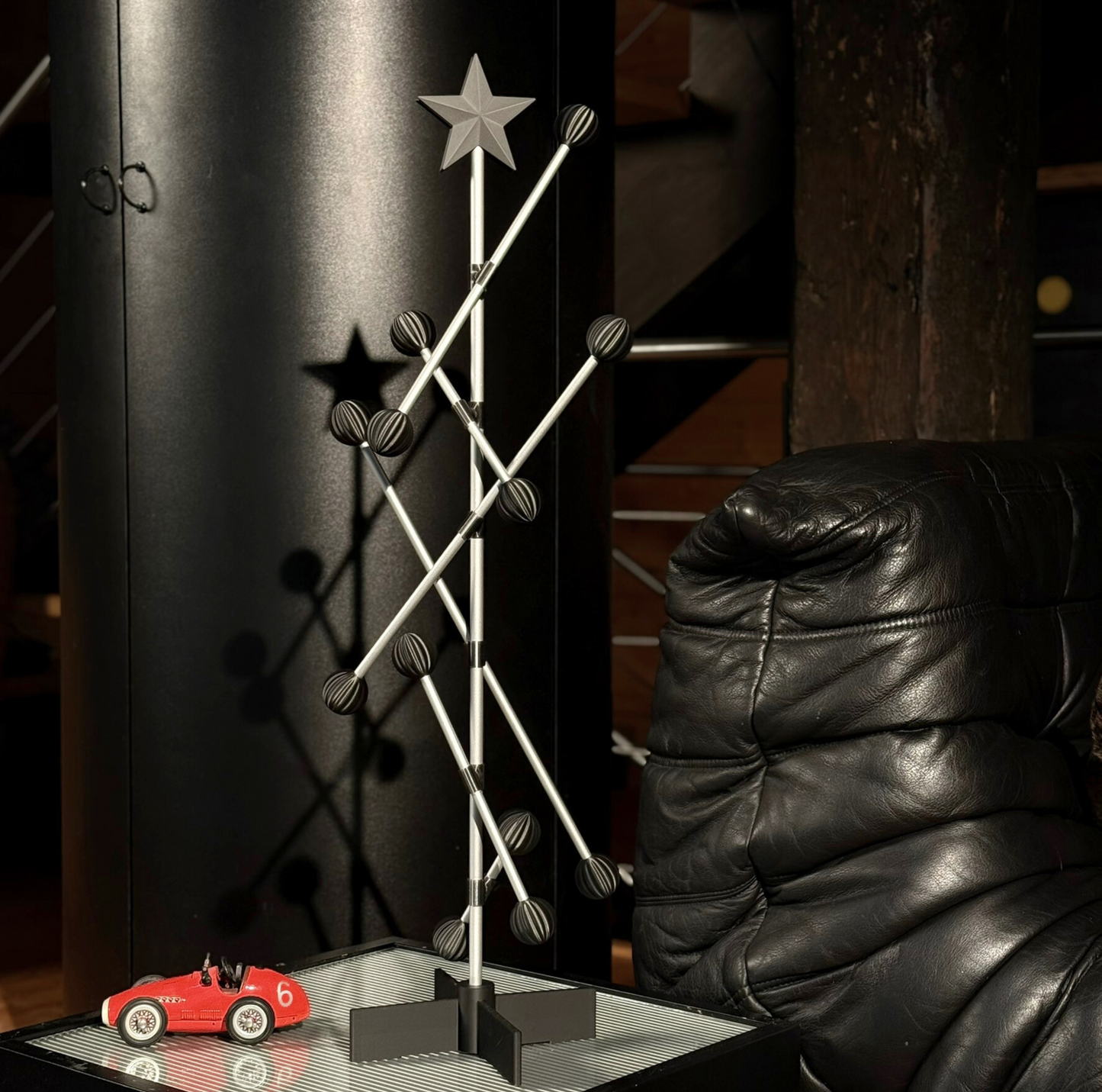 Dekorativer Weihnachtsbaum aus Metall mit Stern auf einem Tisch neben einem schwarzen Ledersessel.