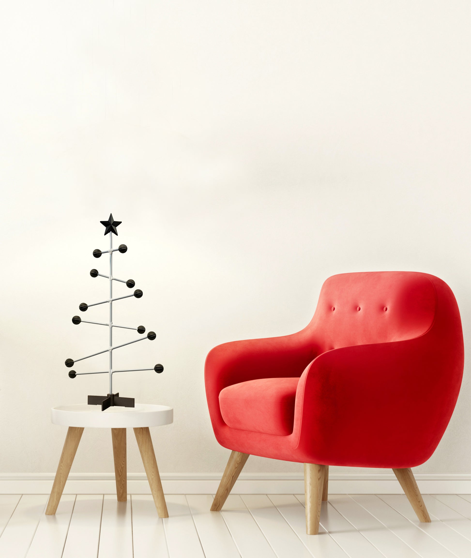 Roter Sessel neben einem kleinen schwarzen Weihnachtsbaum auf einem weißen Hocker vor einer weißen Wand.