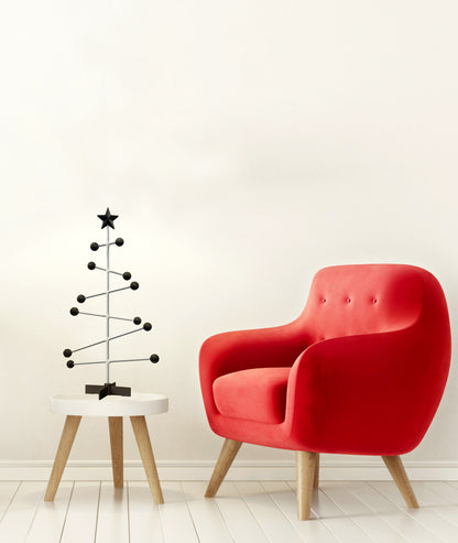 Roter Sessel neben einem kleinen schwarzen Weihnachtsbaum auf einem weißen Hocker vor einer weißen Wand.