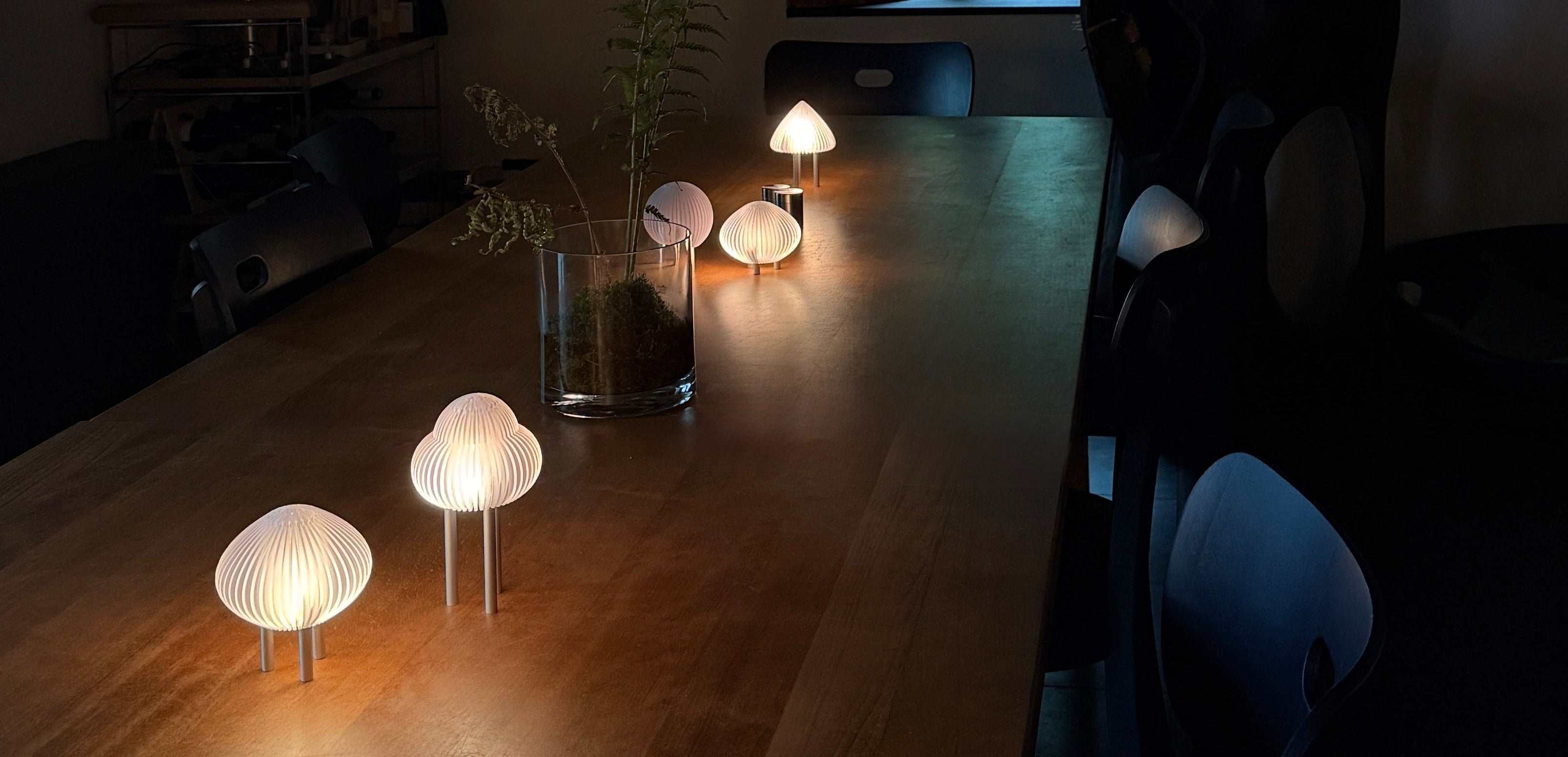 Dining room with wooden table and chairs, illuminated by small round lamps.