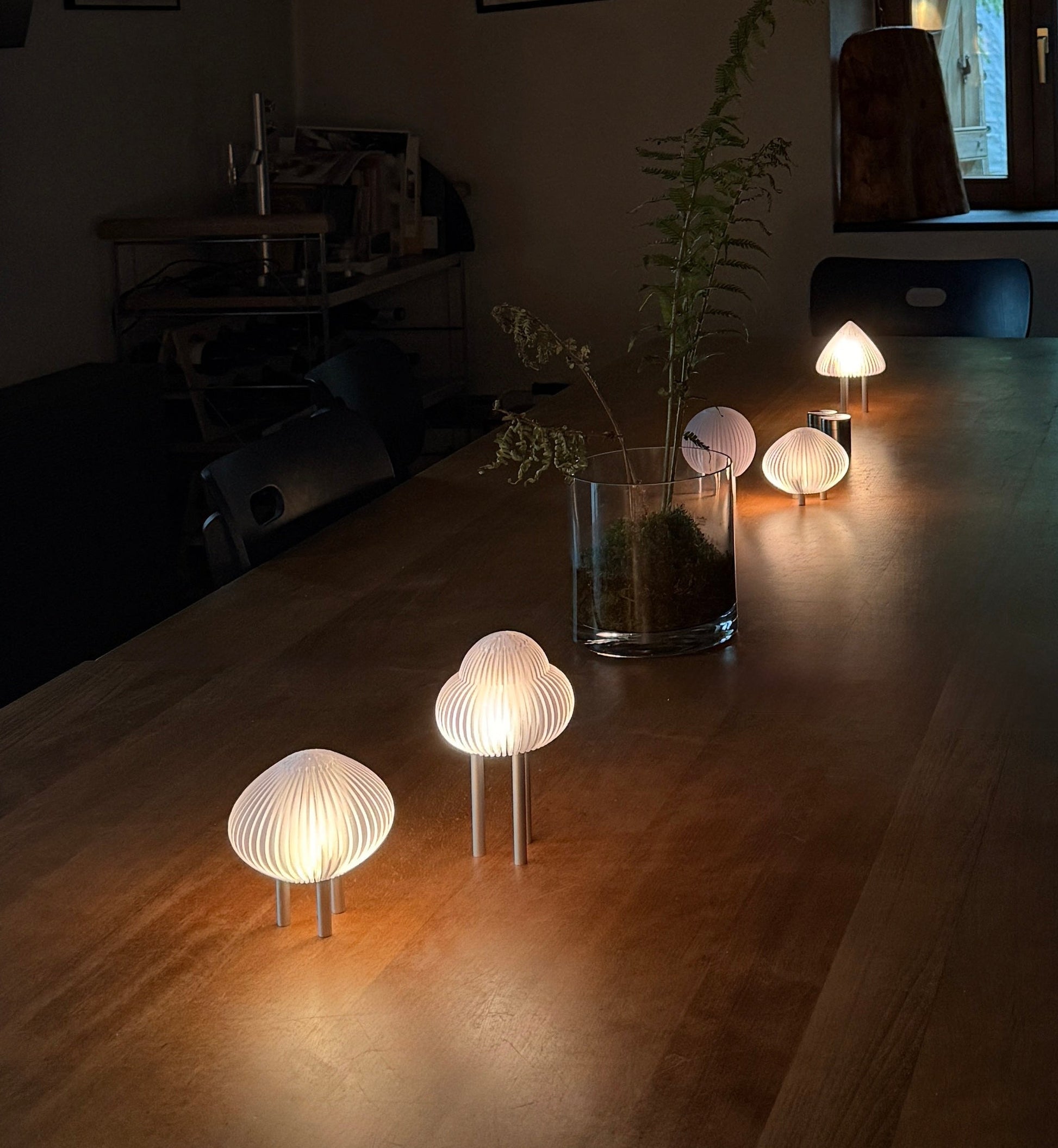 Dining room with wooden table and chairs, illuminated by small round lamps.