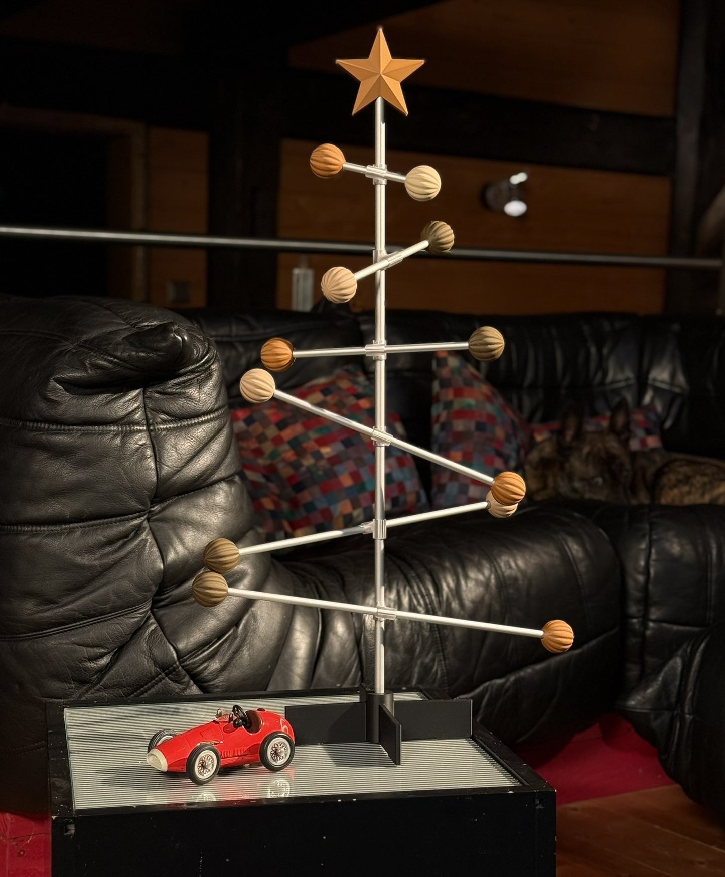 Decorative wooden and metal Christmas tree with a red car on a stand in a living room setting.
