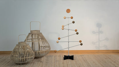 Dekorativer Metallbaum mit Holzball-Ornamenten vor einem einfarbigen Wandhintergrund