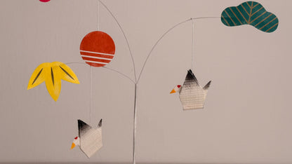 Colorful paper mobile with flowers, leaves, and birds on a plain background