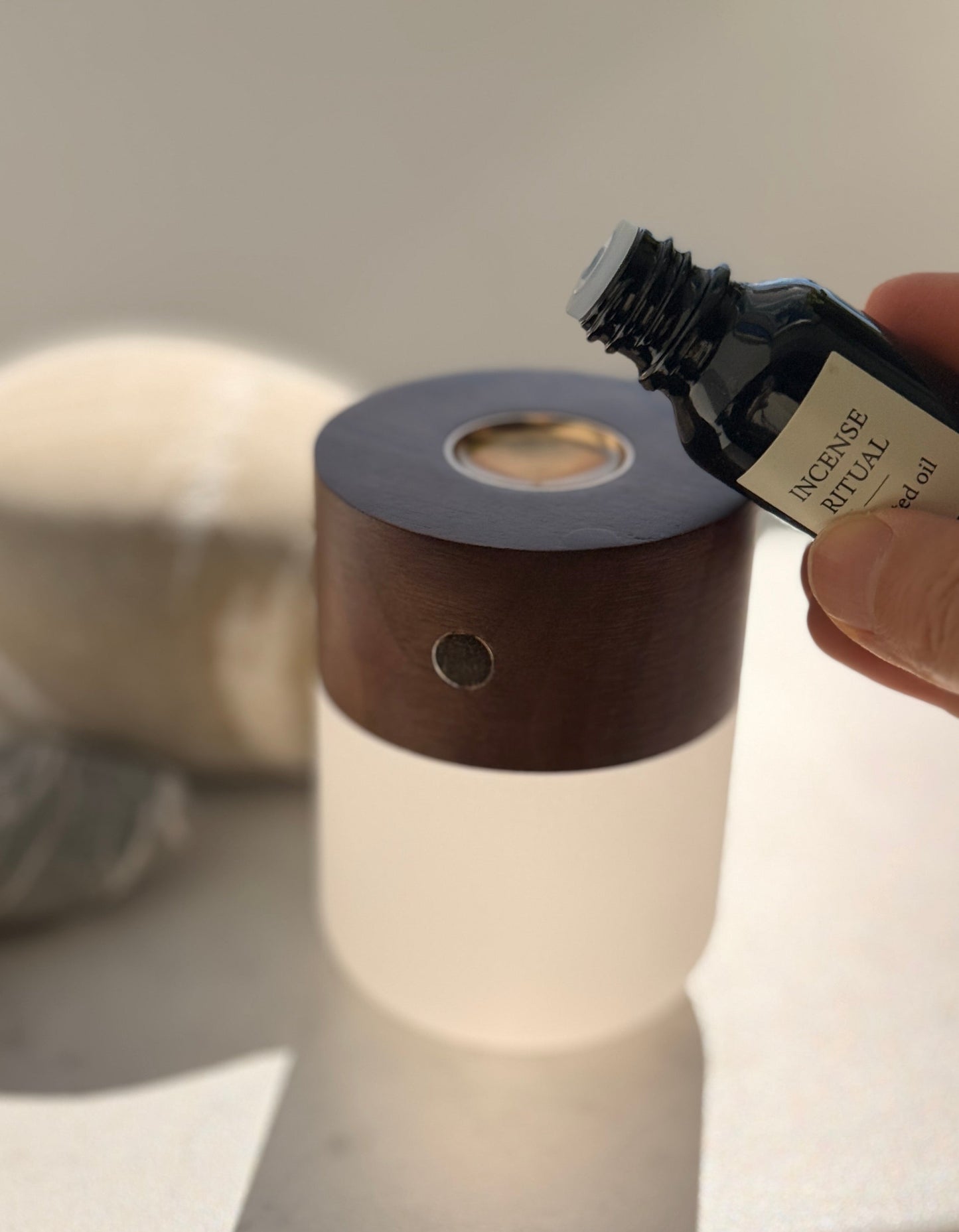 Person pouring essential oil into a diffuser on a light surface