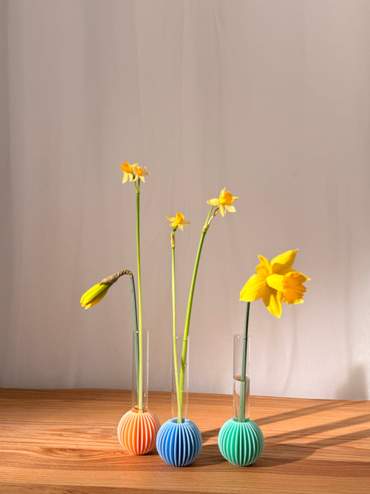Yellow flowers in a vase on a wooden surface with colorful spherical objects.