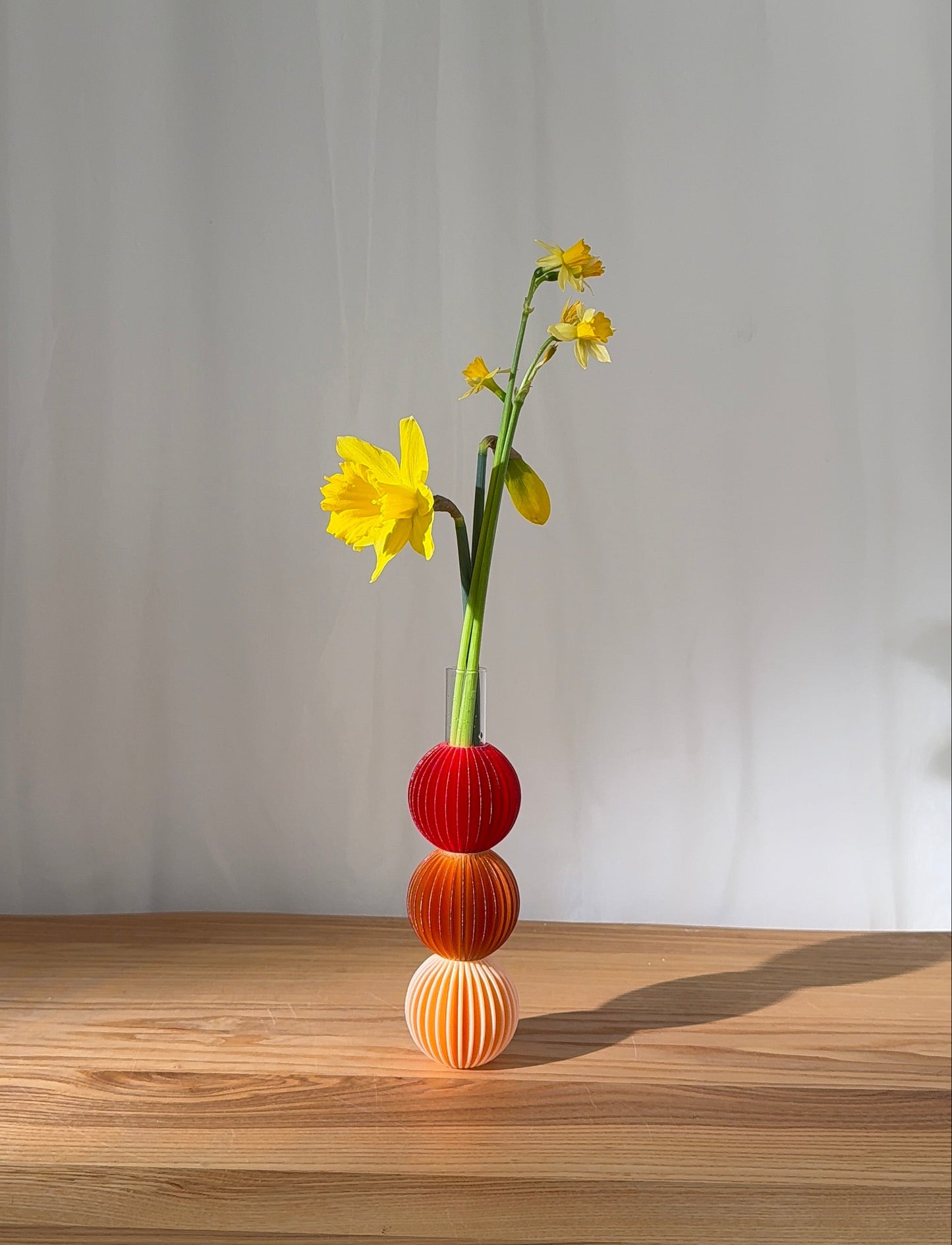 Three-tiered vase with yellow flowers on a wooden surface against a gray wall