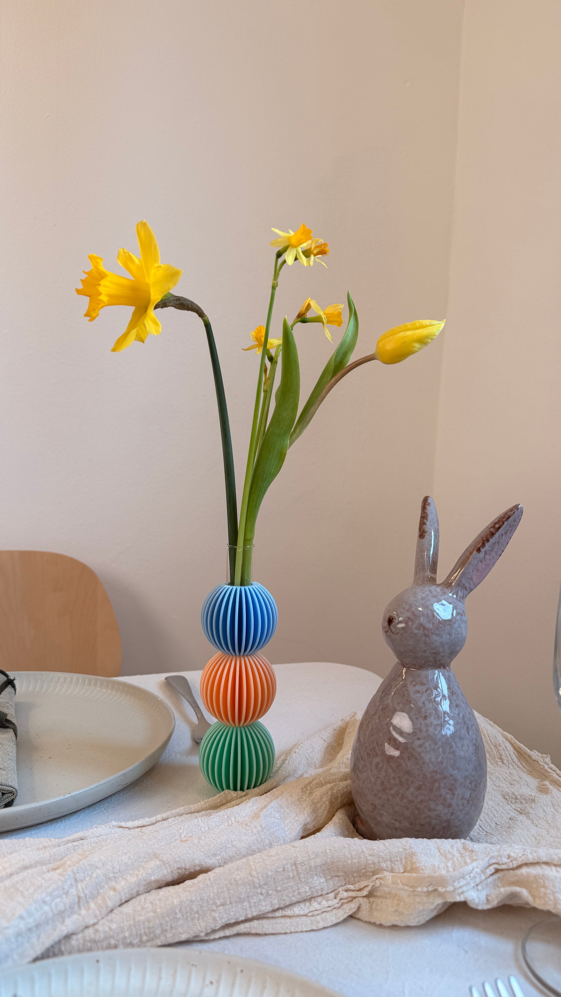 Decorative setup with a vase of yellow flowers, colorful spherical objects, and a rabbit-shaped figurine on a table.