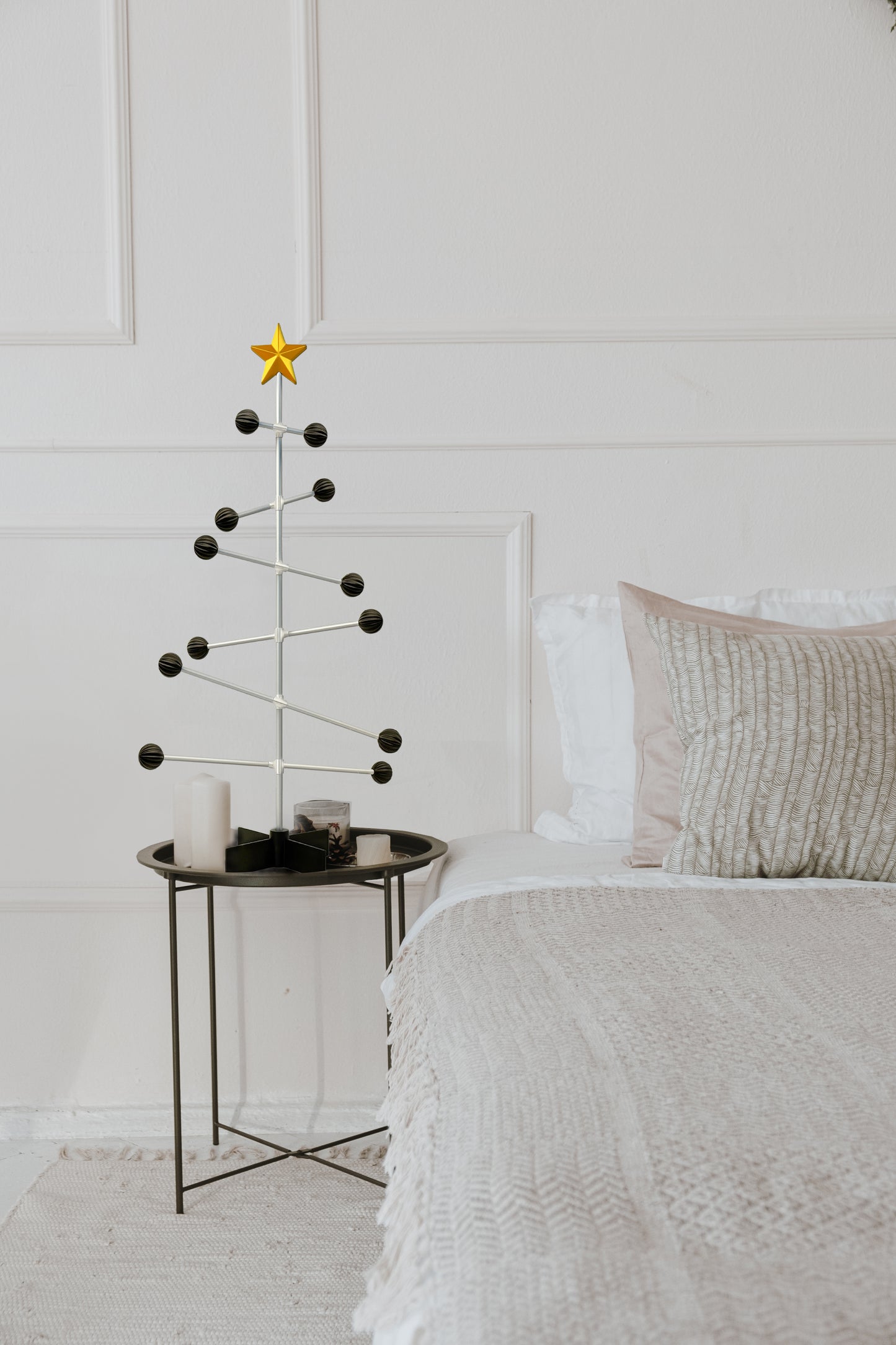 Minimalist Christmas tree with a star on a small table next to a bed in a bedroom.
