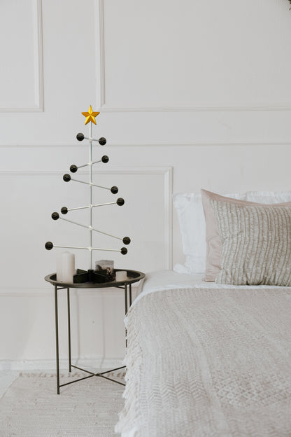 Minimalist Christmas tree with a star on a small table next to a bed in a bedroom.