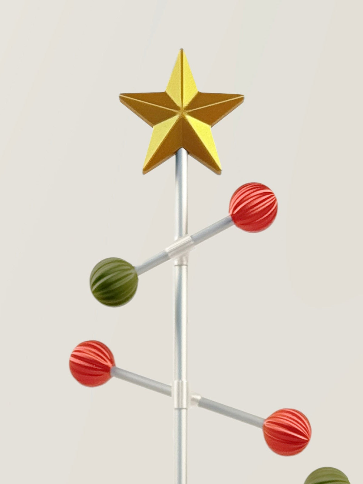 Decorative metal Christmas tree with red and green ball and a gold star on top against a light gray background