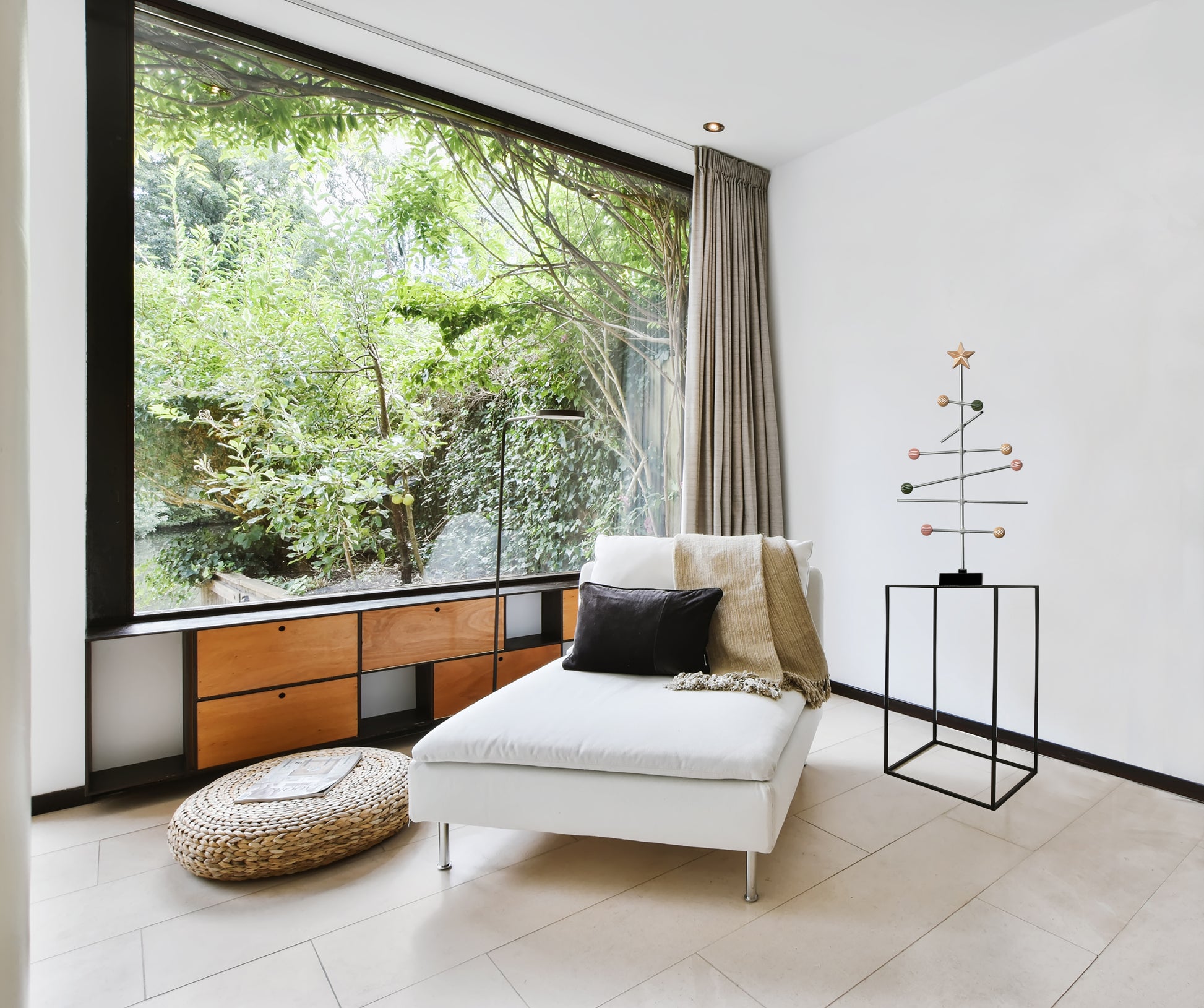 Modern living room with a large window, white sofa, and a modular pastel spring colored tree stand on the shelf